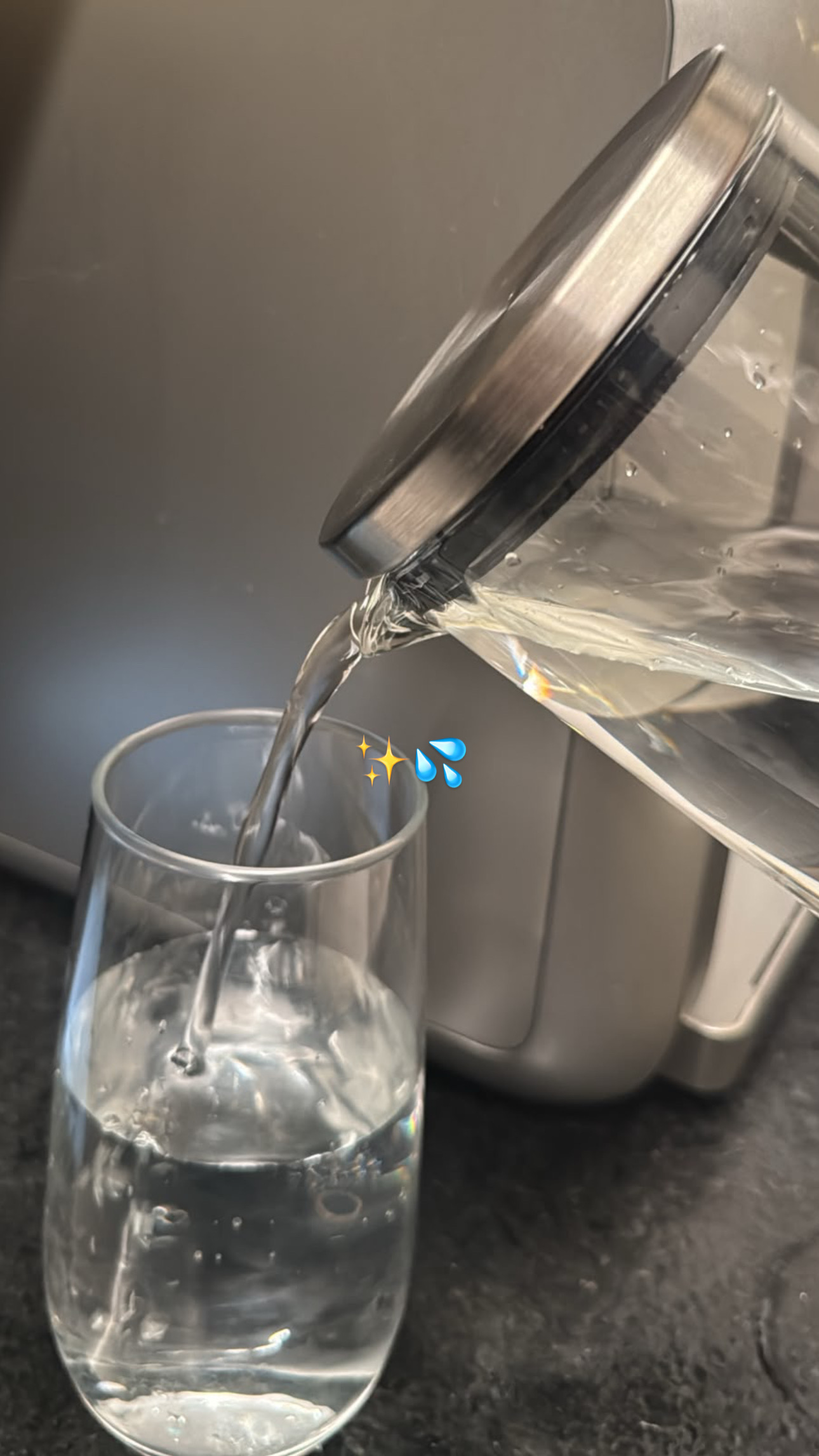 Uma pessoa está despejando água de um recipiente em um copo transparente sobre uma superfície escura.